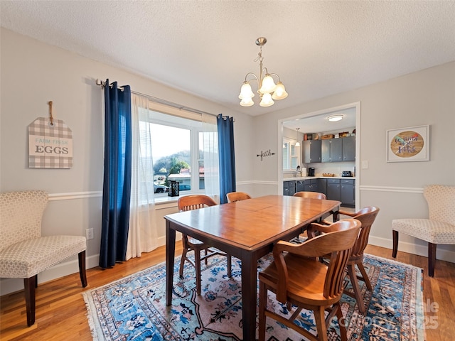 dining room featuring baseboards, a notable chandelier, light wood-type flooring, and a textured ceiling