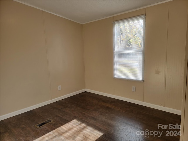 empty room featuring dark wood-type flooring and ornamental molding