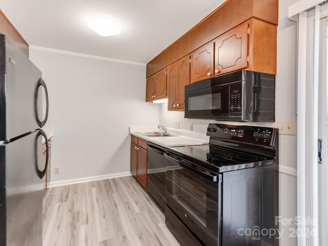 kitchen with black appliances, ornamental molding, sink, and light hardwood / wood-style flooring