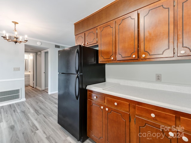 kitchen featuring an inviting chandelier, black fridge, crown molding, pendant lighting, and light hardwood / wood-style floors