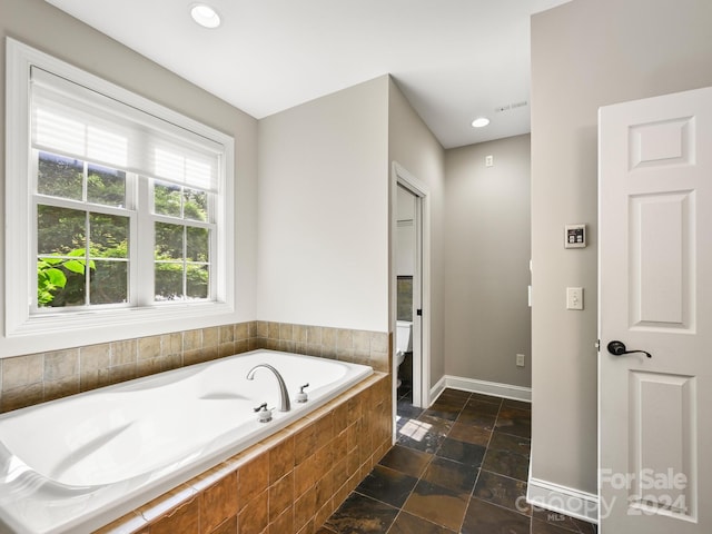 bathroom with a relaxing tiled tub and toilet