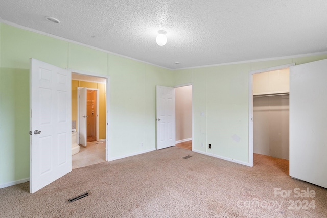 unfurnished bedroom featuring light carpet, a textured ceiling, crown molding, a spacious closet, and a closet