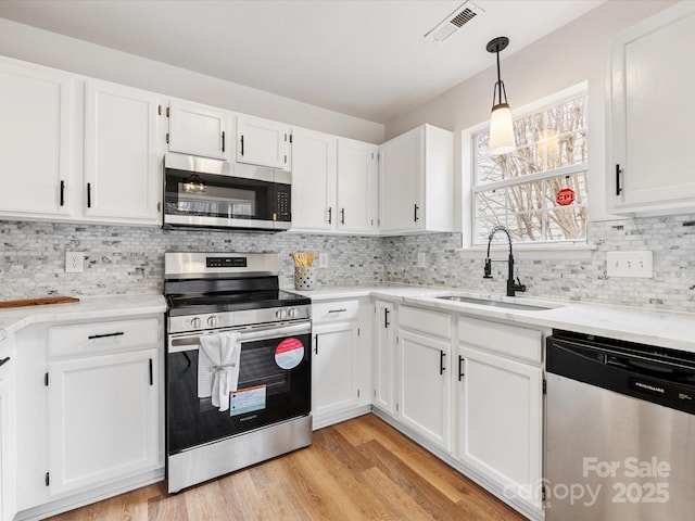 kitchen featuring appliances with stainless steel finishes, pendant lighting, white cabinetry, sink, and light hardwood / wood-style floors