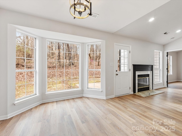 unfurnished dining area with an inviting chandelier, a premium fireplace, and light wood-type flooring