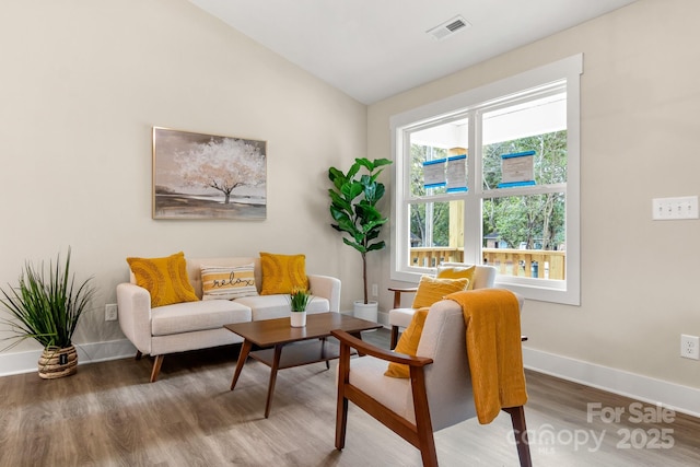 sitting room with plenty of natural light, lofted ceiling, and hardwood / wood-style flooring