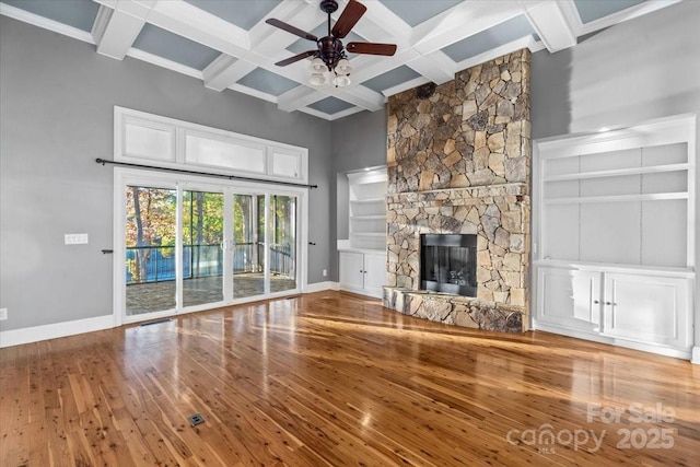 unfurnished living room with coffered ceiling, ceiling fan, beam ceiling, hardwood / wood-style floors, and a stone fireplace