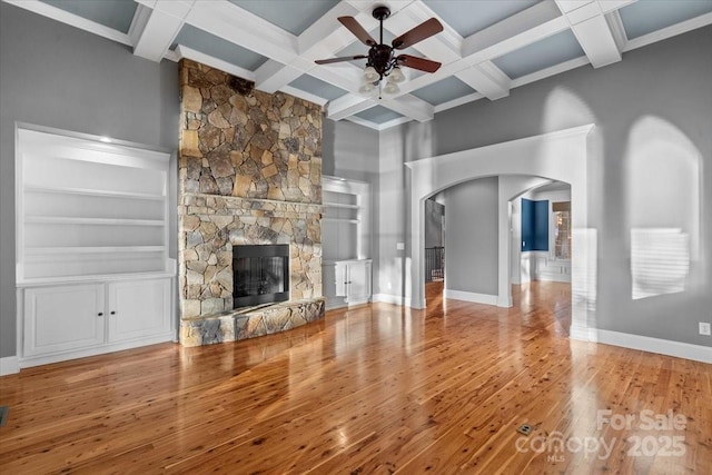 unfurnished living room featuring coffered ceiling, ceiling fan, hardwood / wood-style flooring, built in features, and a stone fireplace