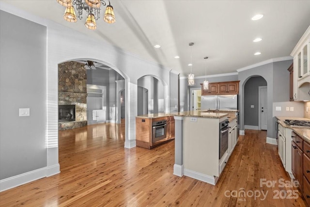 kitchen featuring a center island with sink, a stone fireplace, hanging light fixtures, and appliances with stainless steel finishes