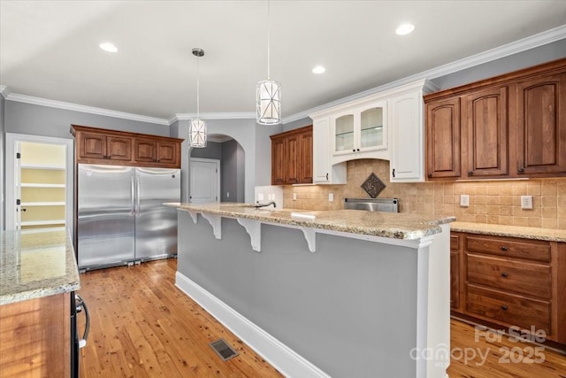 kitchen with a kitchen bar, light wood-type flooring, light stone counters, ornamental molding, and built in refrigerator