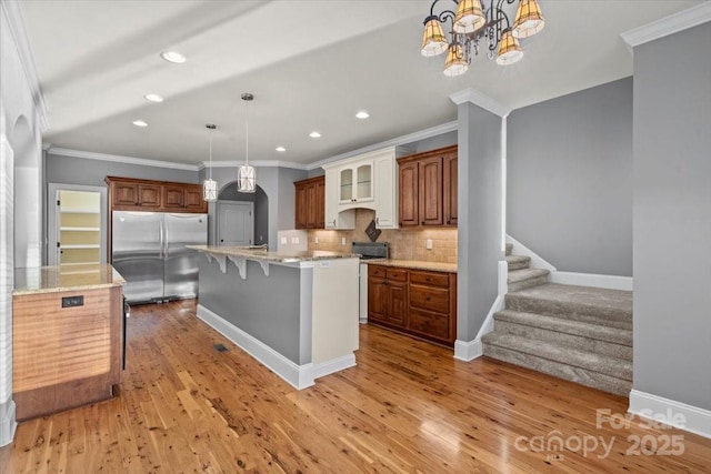 kitchen with backsplash, a center island with sink, decorative light fixtures, a kitchen bar, and stainless steel refrigerator