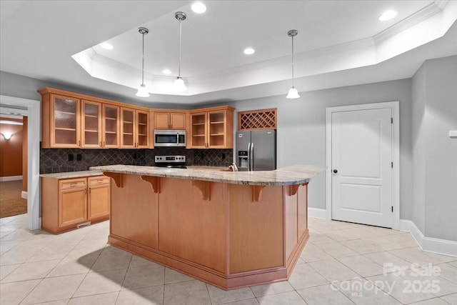 kitchen featuring pendant lighting, a center island with sink, light tile patterned floors, appliances with stainless steel finishes, and a tray ceiling