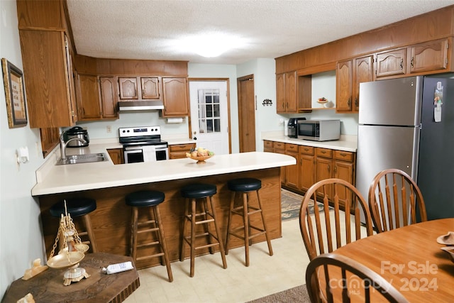 kitchen with a breakfast bar, sink, a textured ceiling, and appliances with stainless steel finishes