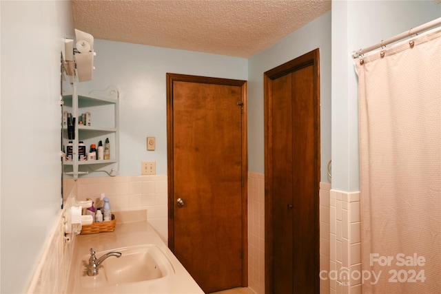 bathroom with a shower with shower curtain, vanity, a textured ceiling, and tile walls