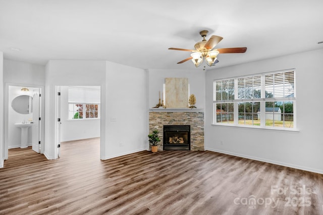 unfurnished living room with ceiling fan, a fireplace, sink, and light wood-type flooring