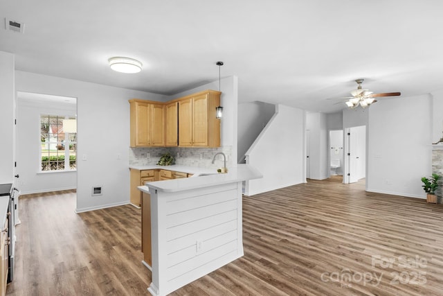 kitchen featuring pendant lighting, sink, backsplash, light brown cabinetry, and kitchen peninsula