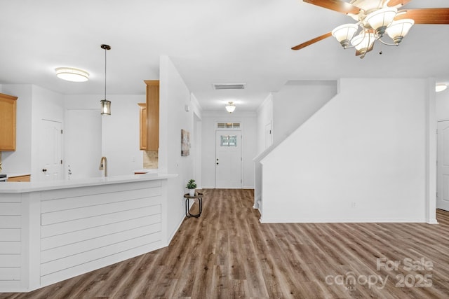 kitchen with light brown cabinetry, wood-type flooring, kitchen peninsula, pendant lighting, and ceiling fan