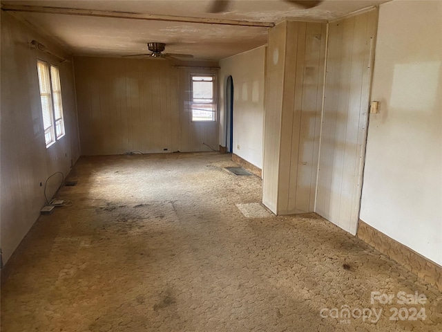 carpeted spare room featuring wooden walls and ceiling fan