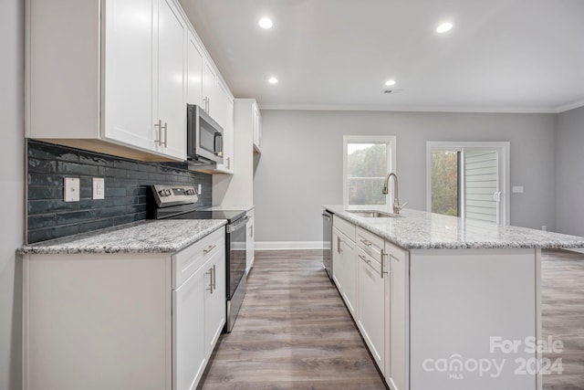 kitchen with light stone countertops, appliances with stainless steel finishes, sink, white cabinets, and an island with sink