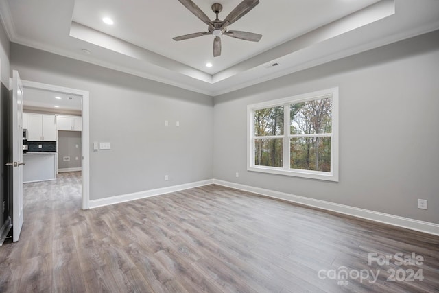 spare room with a tray ceiling, ceiling fan, and light hardwood / wood-style floors