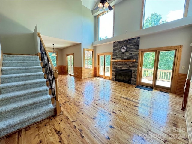 unfurnished living room featuring ceiling fan, a healthy amount of sunlight, a stone fireplace, and a high ceiling