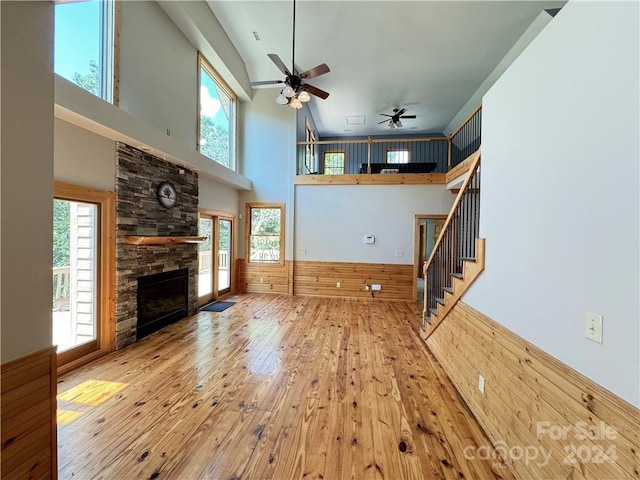 unfurnished living room featuring ceiling fan, a high ceiling, wood walls, a fireplace, and hardwood / wood-style flooring