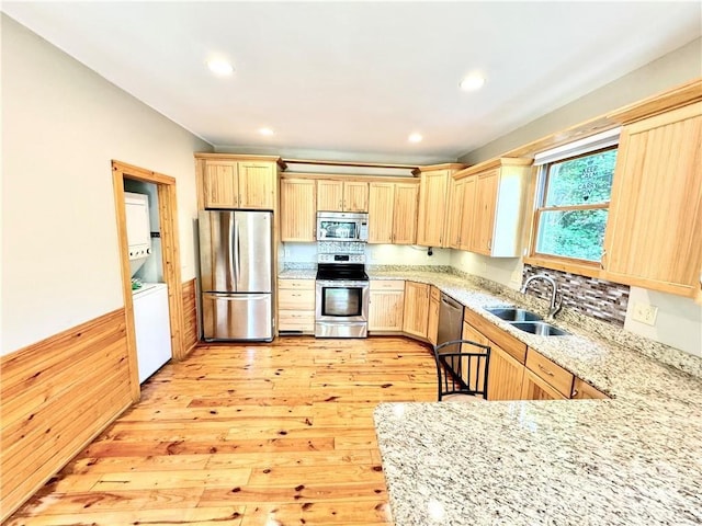 kitchen with light brown cabinets, sink, stacked washer and dryer, light hardwood / wood-style floors, and stainless steel appliances