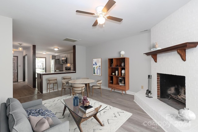 living room featuring light hardwood / wood-style floors, a brick fireplace, and ceiling fan