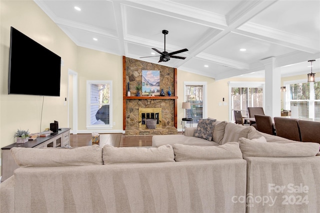 living room with ceiling fan, a stone fireplace, beamed ceiling, wood-type flooring, and ornamental molding