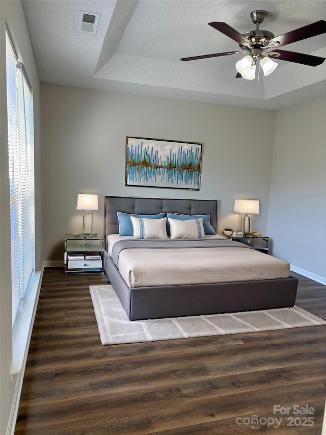 bedroom with a textured ceiling, dark hardwood / wood-style flooring, a raised ceiling, and ceiling fan