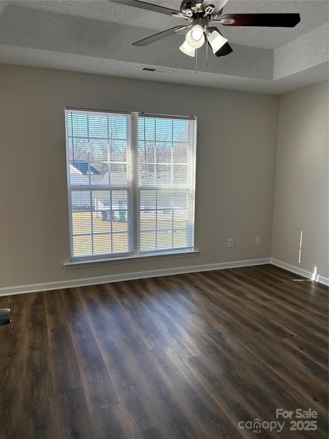 empty room featuring ceiling fan, dark hardwood / wood-style floors, a textured ceiling, and a tray ceiling