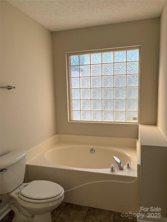 bathroom featuring tile patterned floors, a bathing tub, a textured ceiling, and toilet