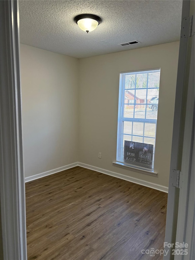 empty room with a textured ceiling and dark hardwood / wood-style flooring