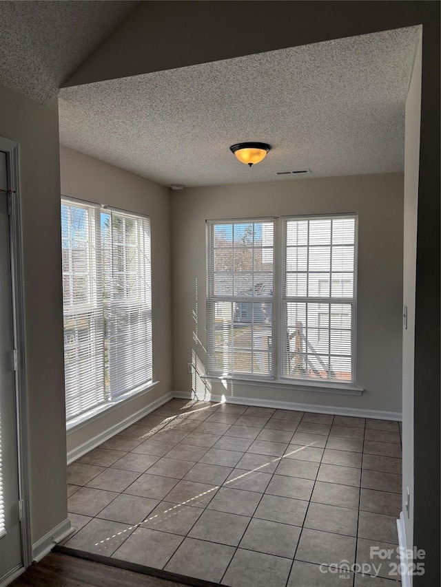 unfurnished dining area with tile patterned flooring, a textured ceiling, and lofted ceiling