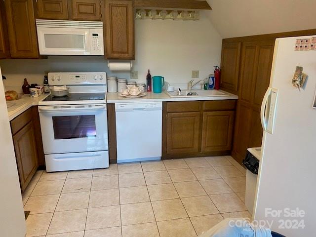 kitchen with light tile patterned floors, white appliances, vaulted ceiling, and sink