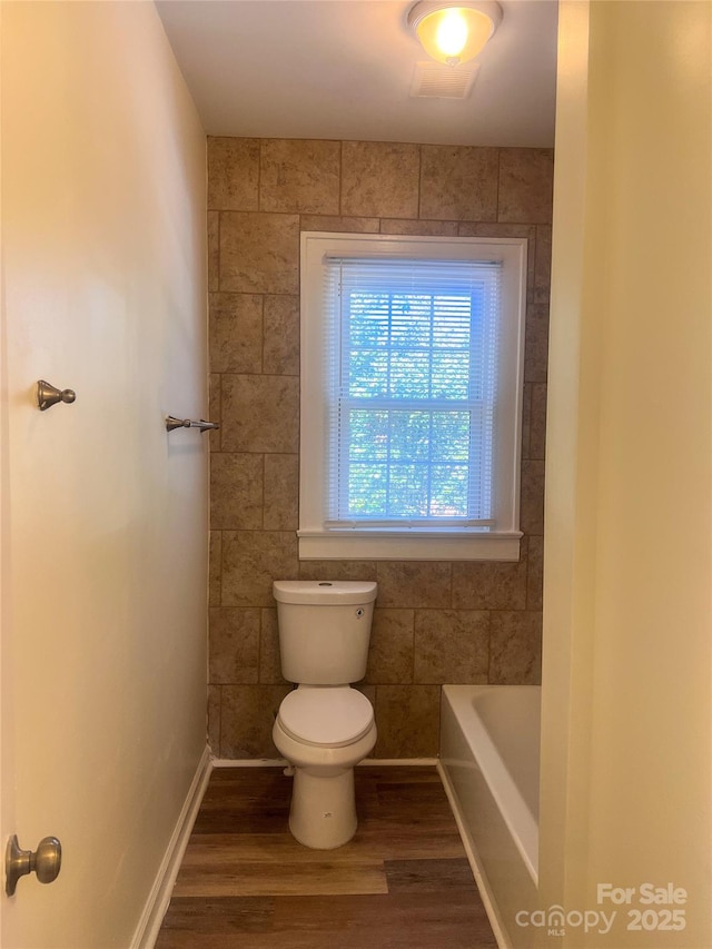 bathroom with a bathing tub, toilet, baseboards, and wood finished floors