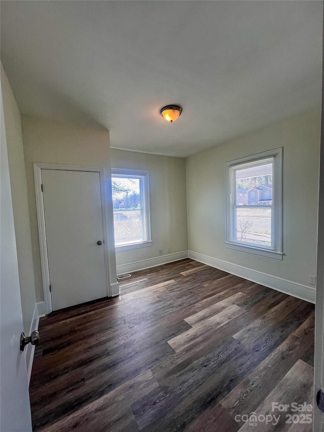 spare room featuring visible vents, baseboards, and dark wood-style floors