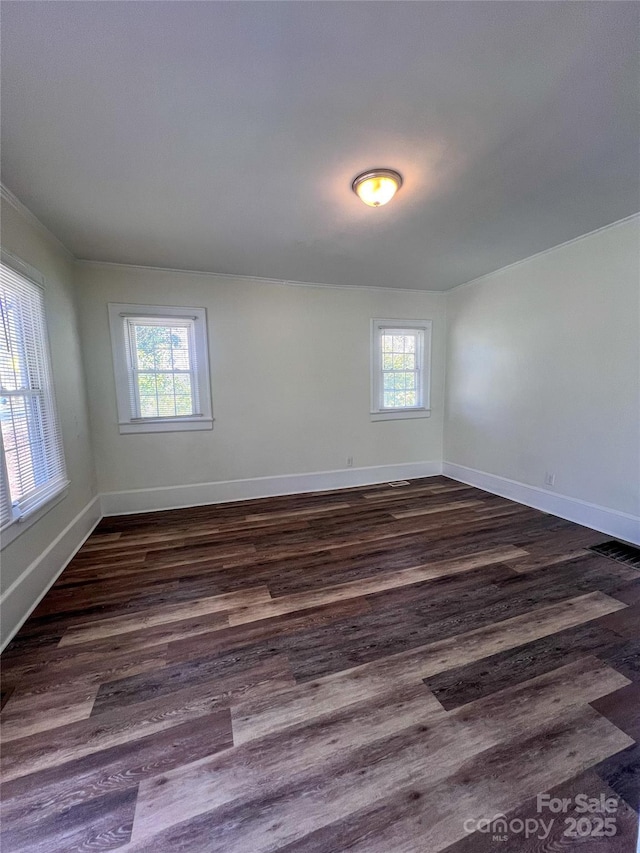 empty room with dark wood finished floors, baseboards, and a wealth of natural light