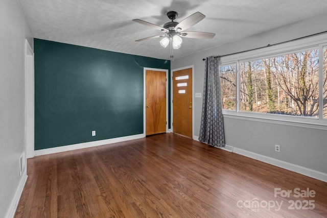 spare room with visible vents, wood finished floors, a ceiling fan, and baseboards