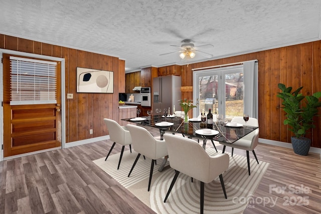 dining room with light wood-style floors, ceiling fan, a textured ceiling, and baseboards