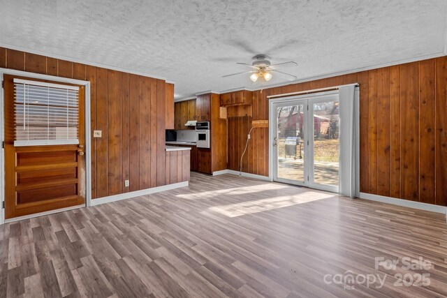 unfurnished living room with ceiling fan, a textured ceiling, baseboards, and wood finished floors