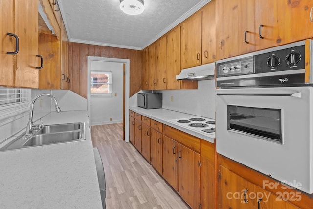 kitchen featuring white appliances, brown cabinetry, ornamental molding, under cabinet range hood, and a sink