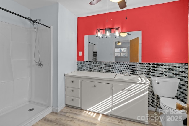 bathroom featuring a ceiling fan, toilet, wood finished floors, vanity, and a shower stall