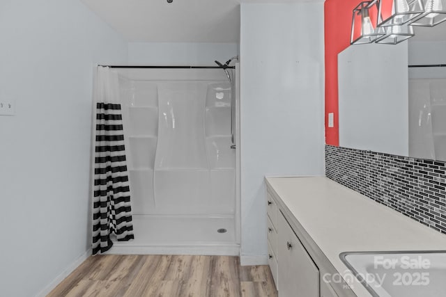 bathroom featuring vanity, a shower stall, decorative backsplash, and wood finished floors