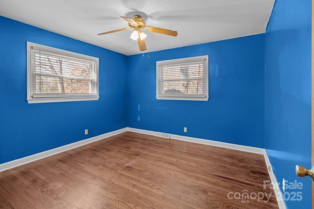 spare room featuring a wealth of natural light, wood finished floors, visible vents, and baseboards