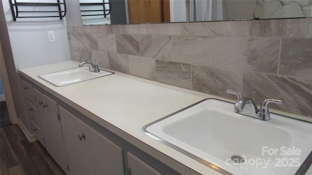 full bath featuring double vanity, decorative backsplash, a sink, and wood finished floors