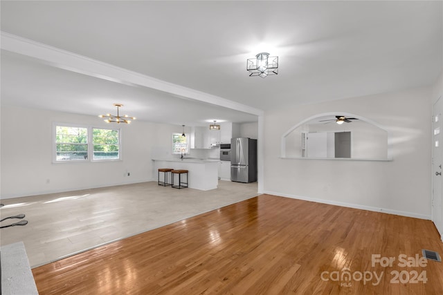 unfurnished living room with ceiling fan with notable chandelier and light wood-type flooring