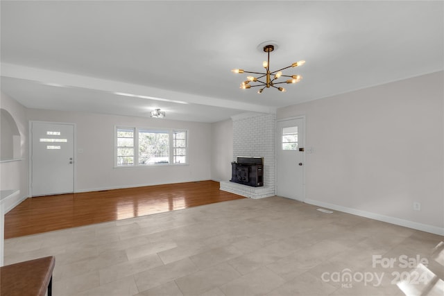 unfurnished living room with a notable chandelier, a wood stove, and light hardwood / wood-style flooring