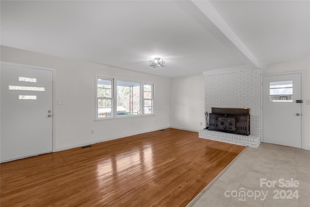 unfurnished living room featuring beamed ceiling, plenty of natural light, light hardwood / wood-style floors, and a fireplace