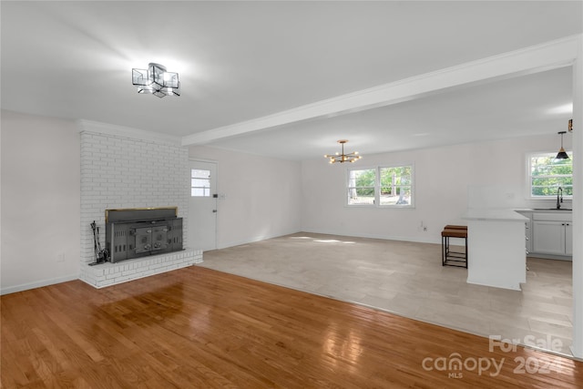 unfurnished living room featuring beam ceiling, plenty of natural light, light hardwood / wood-style floors, and a notable chandelier