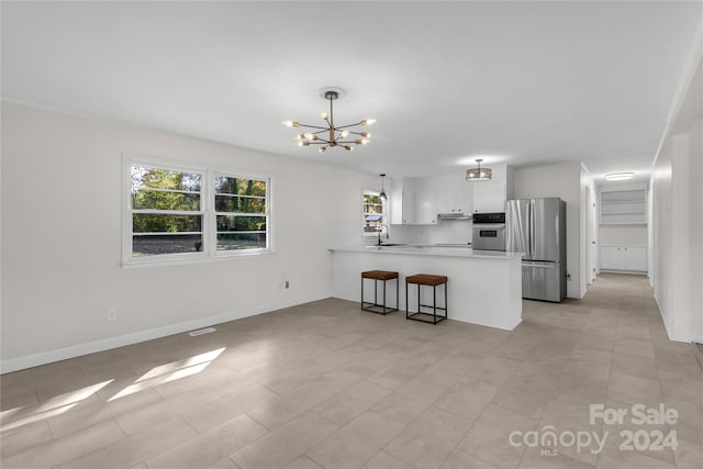 kitchen featuring kitchen peninsula, appliances with stainless steel finishes, decorative light fixtures, a chandelier, and white cabinetry